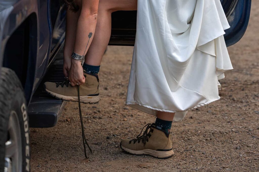 A bride in her wedding dress laces up her hiking boots during her adventure elopement.