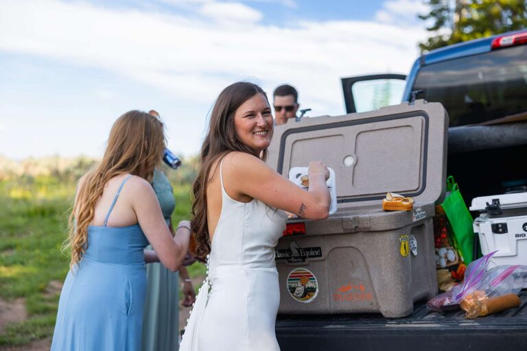 A bride digs in a cooler during a tailgate lunch on her adventure elopement near Meadowlark Lake in Wyoming.