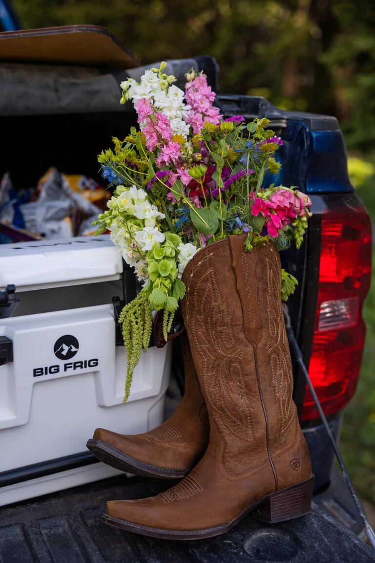 Cowgirl boots full of wildflowers it in front of a cooler in the bed of a pickup truck during a tailgate wedding lunch near Meadowlark Lake in Wyoming.