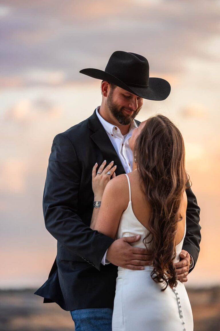 A bride and groom smile at one another in front of a beautiful sunset during their western-inspired wedding in Wyoming.