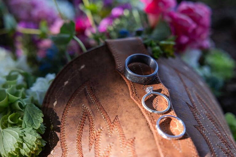 Three wedding rings sit on top of a cowboy boot with a bouquet of wildflowers during a western-inspired Wyoming wedding.