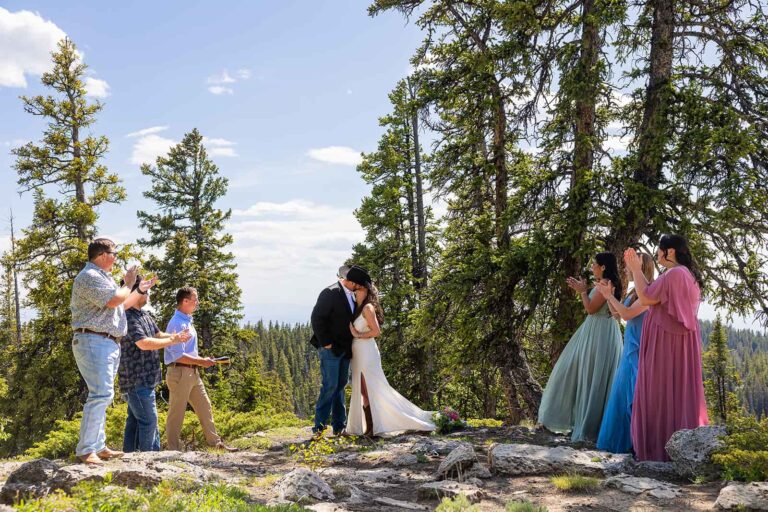 A small group of people gather around a bride and groom during their intimate wedding ceremony in the mountains for a Meadowlark Lake wedding in Wyoming.