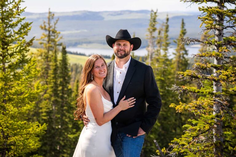 A couple smile at the camera while standing in front of Meadowlark Lake during their adventure elopement in Wyoming.