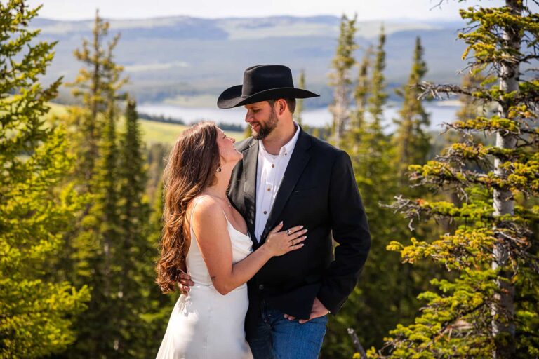 Standing in front of Meadowlark Lake, a groom and bride smile at one another during their western-inspired elopement.
