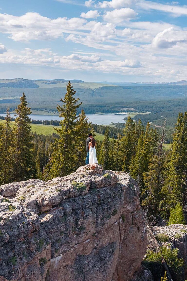 A couple stands on a rocky overlook with views of Meadowlark Lake behind them during their Wyoming Meadowlark Lake Wedding.