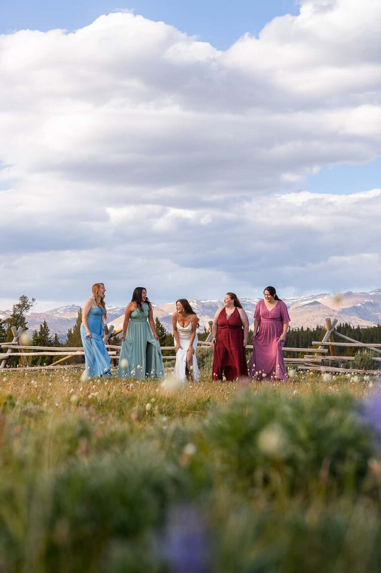 Wearing dresses inspired by the colors of the wildflowers surrounding them, a group of women dance through a meadow during a western style elopement in Wyoming.