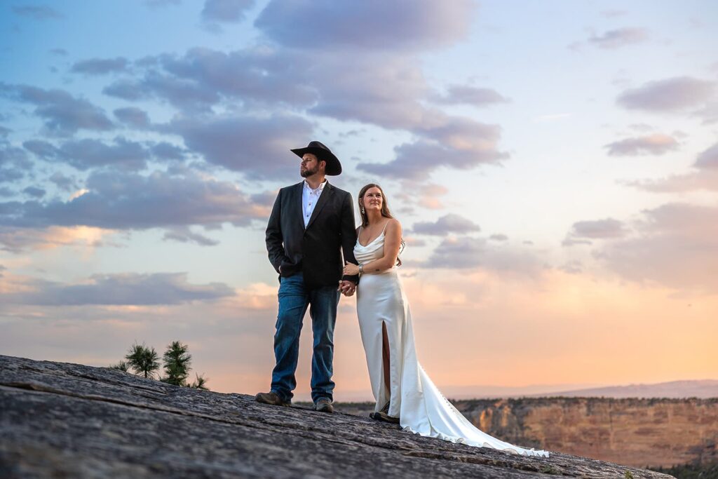A bride and groom pose for a photo in front of a colorful sunset during their western styled Wyoming wedding.