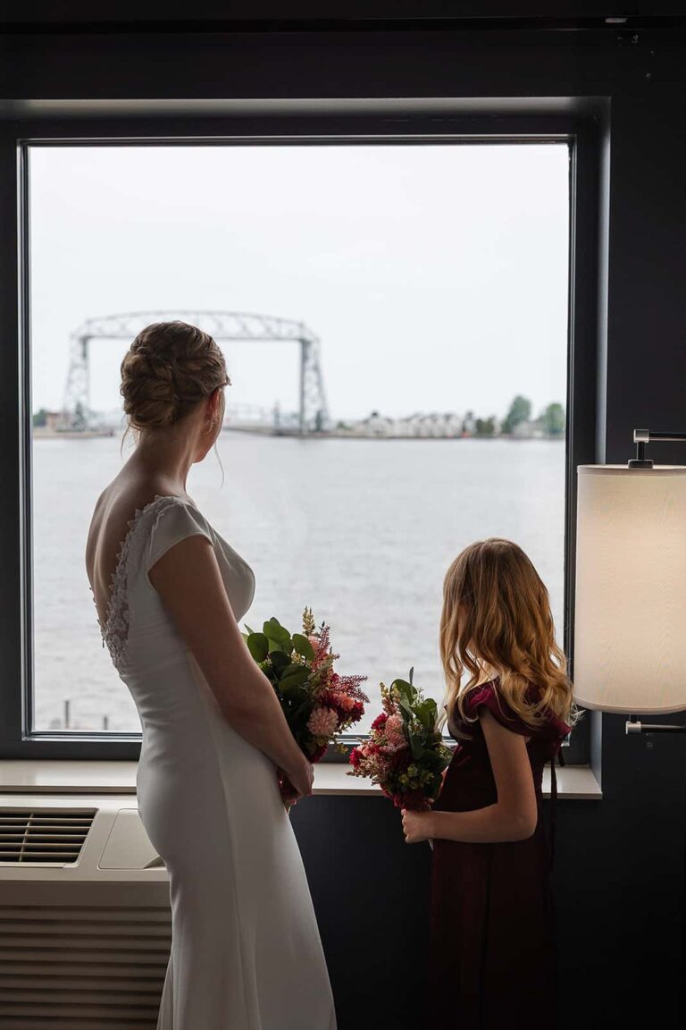 A bride looks out the window at Pier B Resort towards the Duluth Lift bridge on her wedding day.