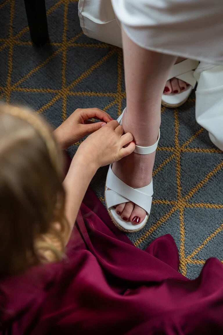A daughter helps her mom put on her wedding shoes on her wedding day at Pier B Resort.