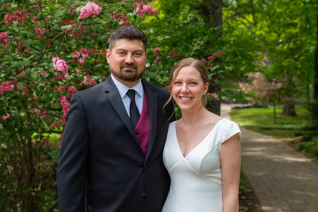 A couple smile at the camera in their wedding clothes during a stroll through a garden near Pier B Resort.