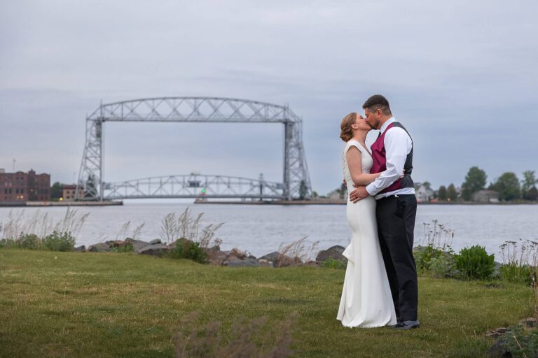 A bride and groom kiss in front of the Duluth Lift Bridge during their wedding.