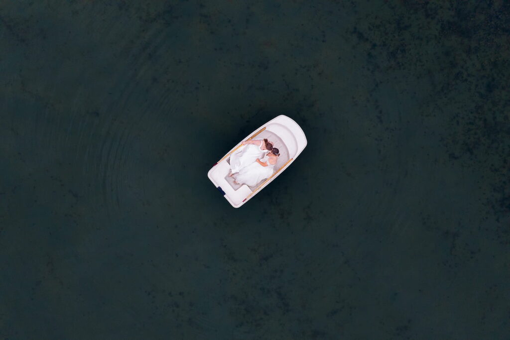 A drone photo of two brides floating in a rowboat sharing a kiss during their elopement with Minnesota elopement photographers, Tali and Dom with Forever and Evergreens.