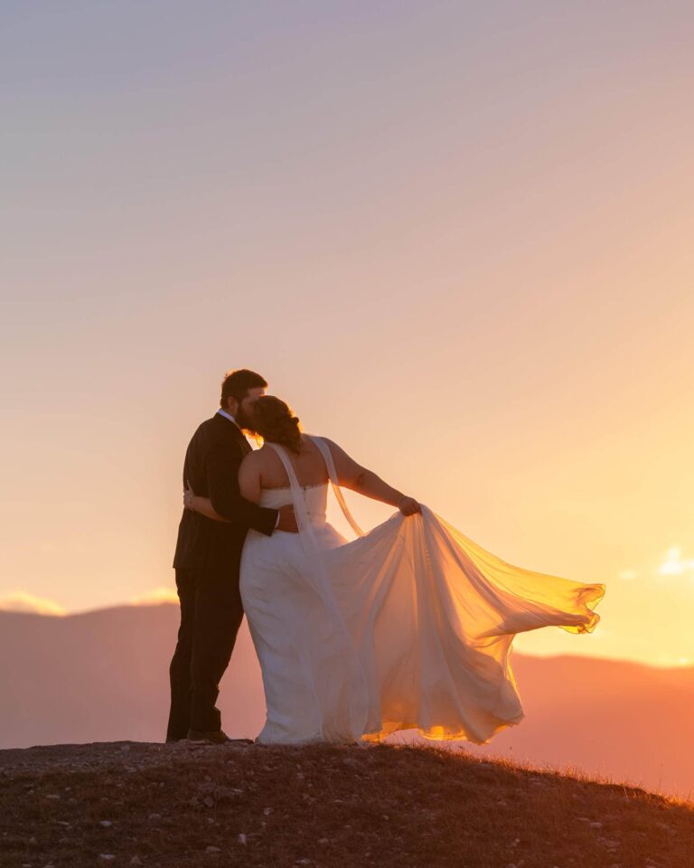 A bride and groom stand in front of a golden mountain sunset during their elopement with Minnesota elopement photographers Forever and Evergreens.