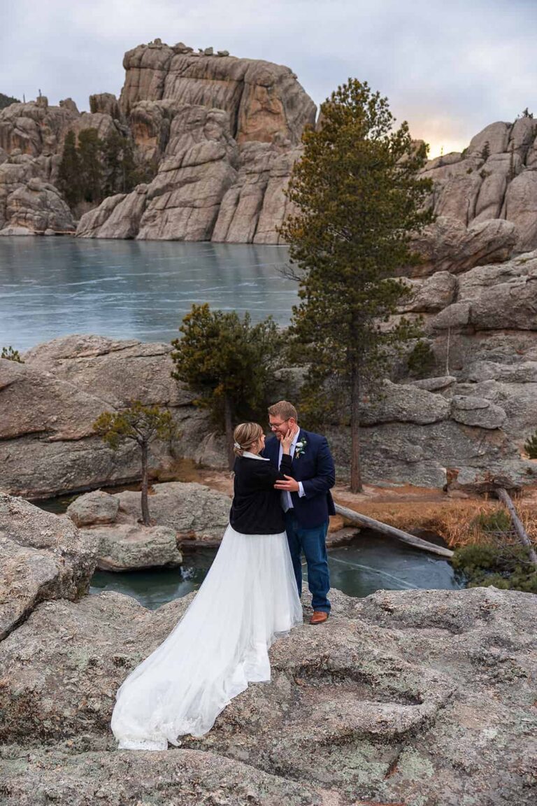 A couple embrace on a jagged rocky cliff in front of a lake during their Midwest elopement with Minnesota elopement photographers, Forever and Evergreens.