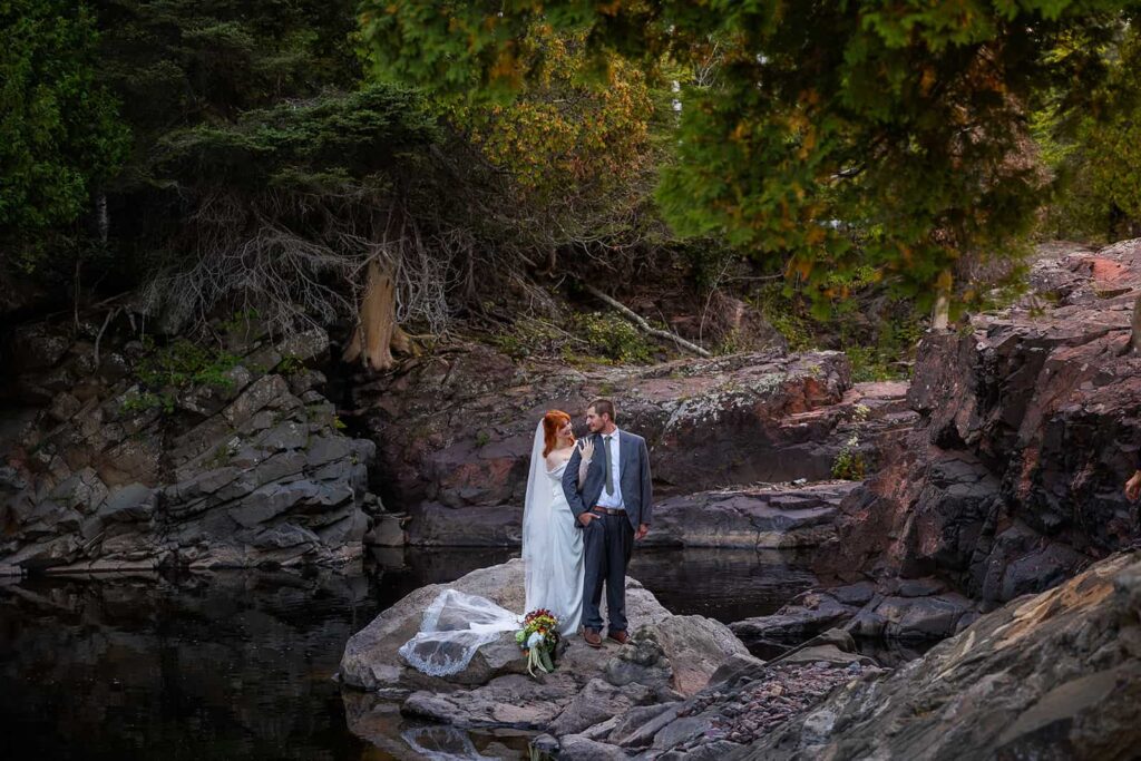 A couple embrace on the bank of a river during their Midwest elopement with Minnesota elopement photographers, Forever and Evergreens.