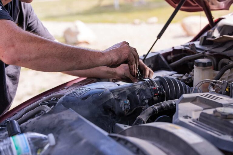 A mans hands hold a wrench as he works on the engine of a truck.
